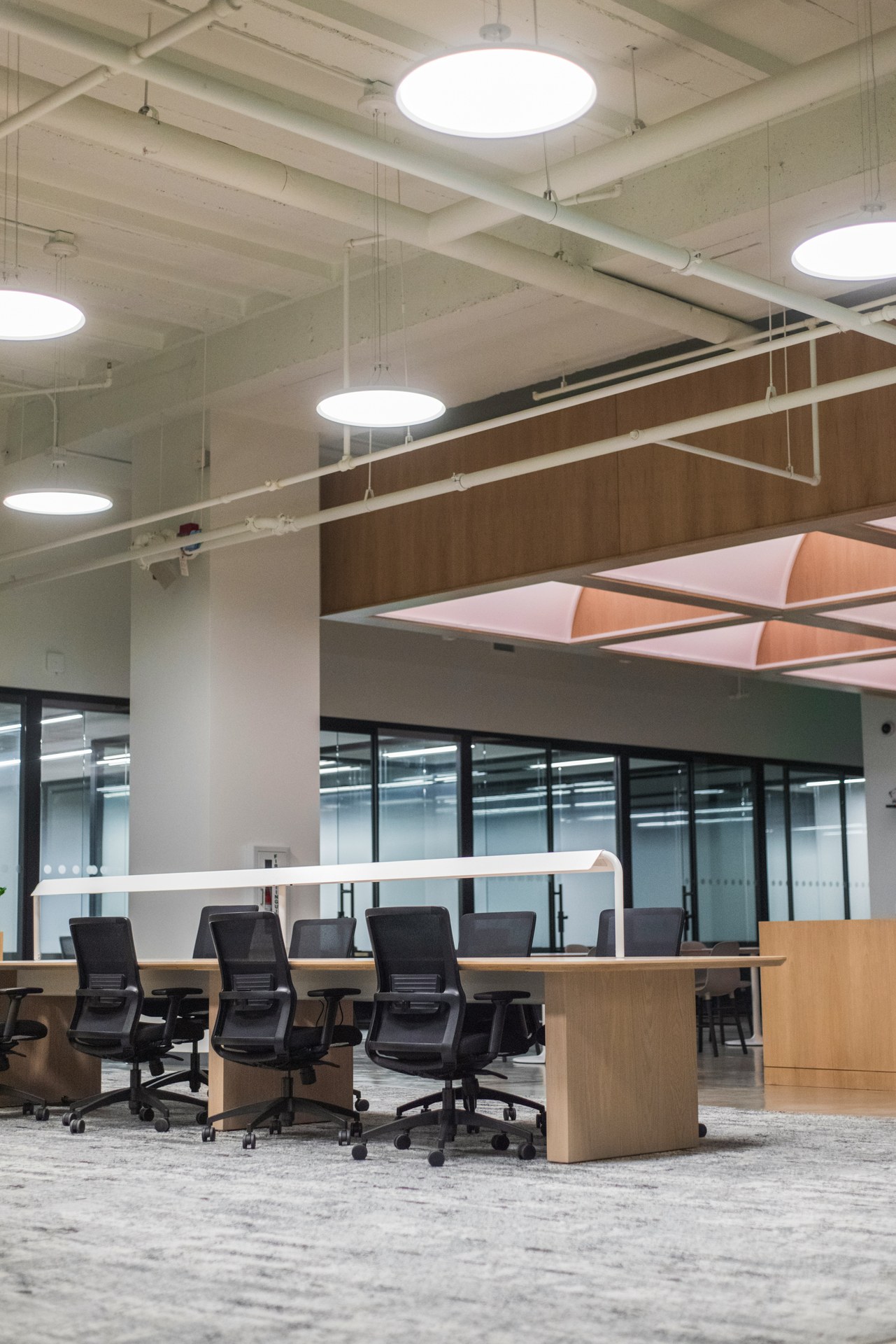 Open-plan office with a shared work table, mesh task chairs, and round pendant lighting under an exposed ceiling, Downtown LA office build-out by ASEP Contractors